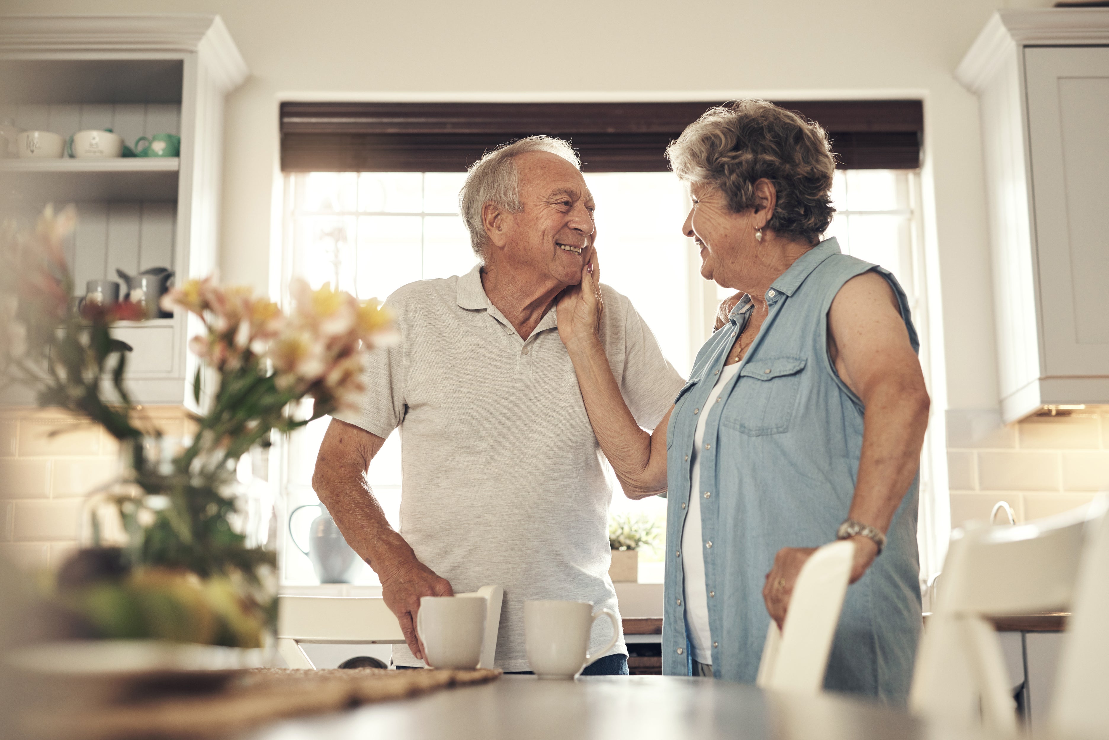 Senior couple standing in a kitchen, smiling at each other.