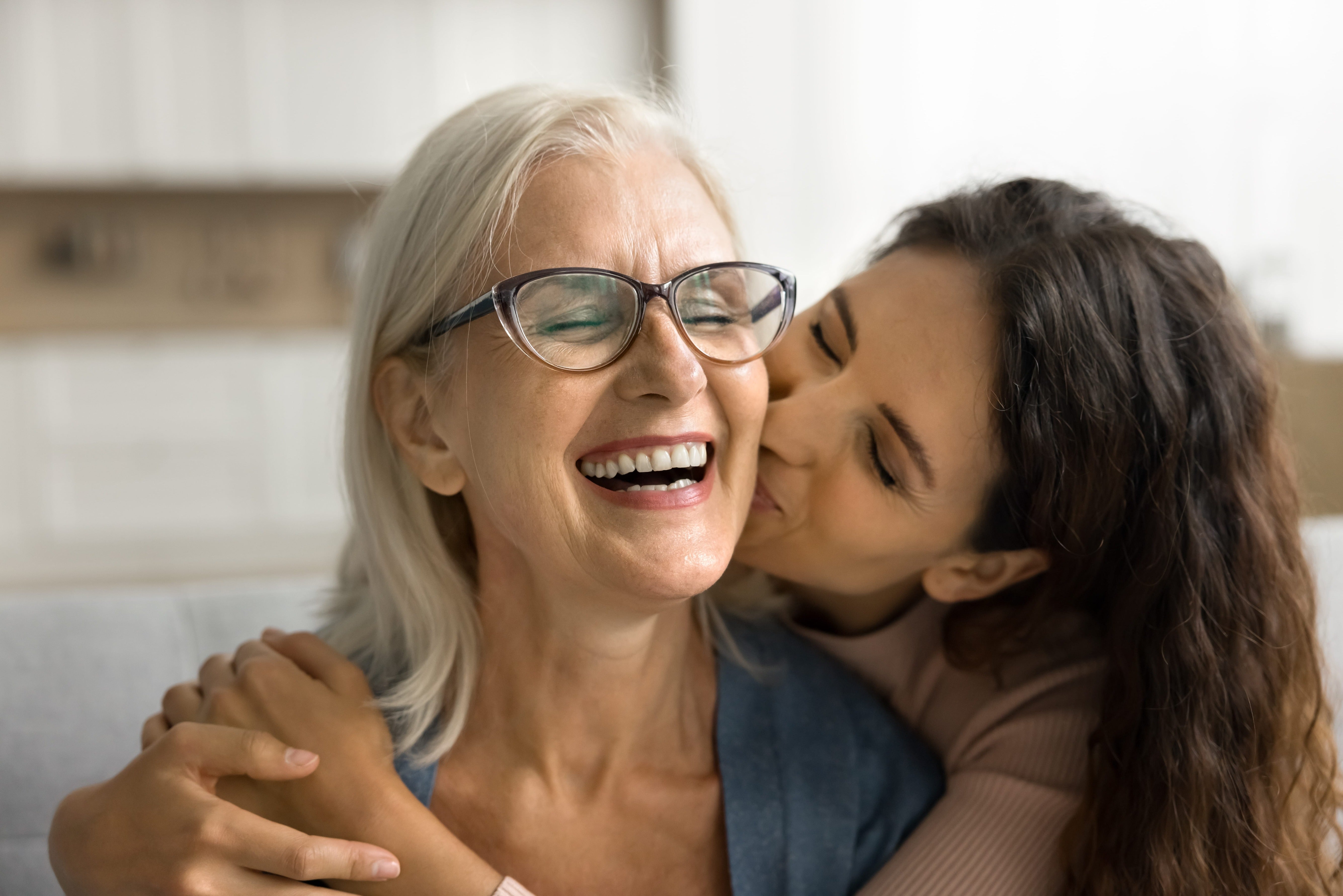 Woman kissing her mother on the cheek in a warm indoor setting