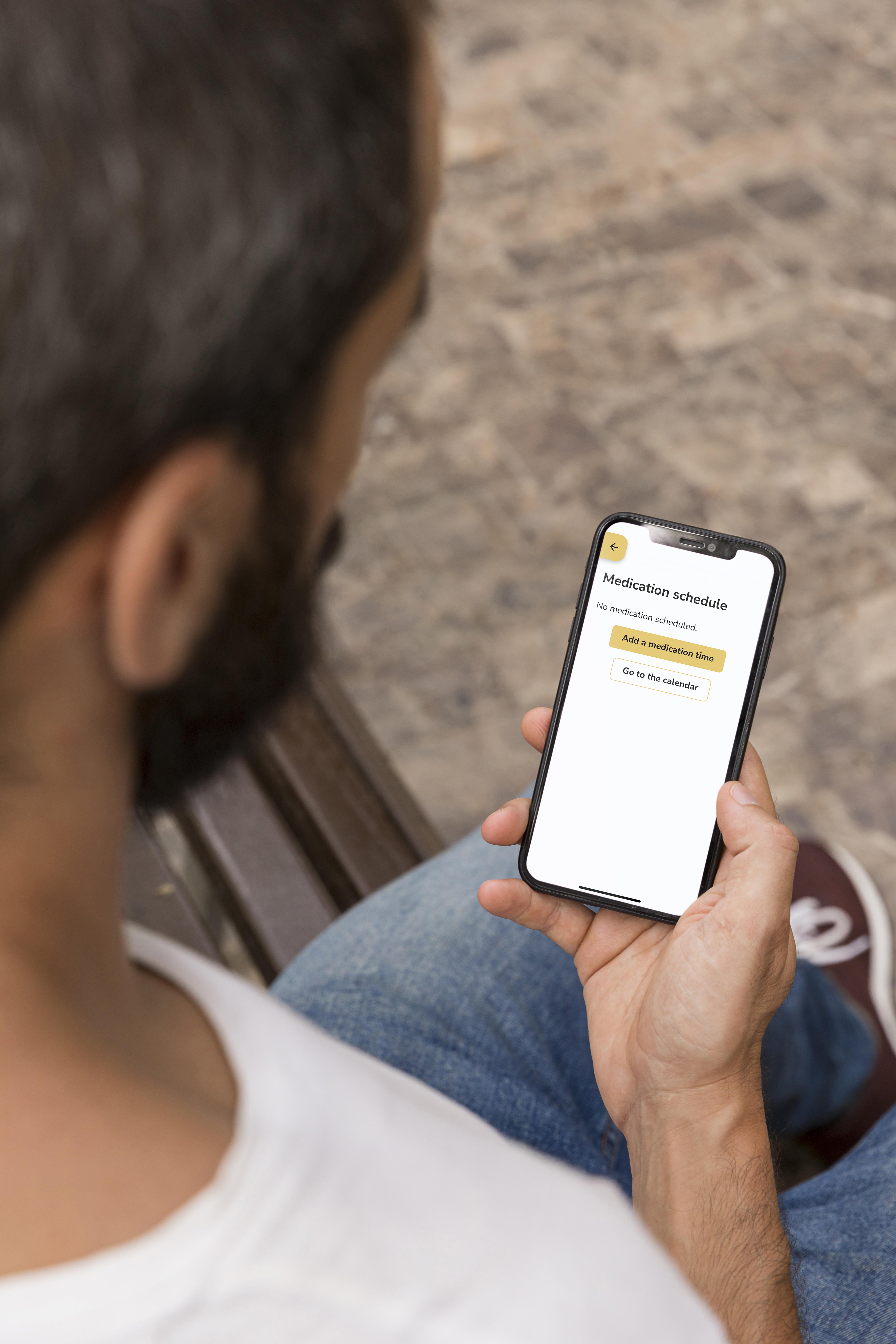 Person holding a smartphone with the Idem Caregiver app on the screen, sitting outdoors.