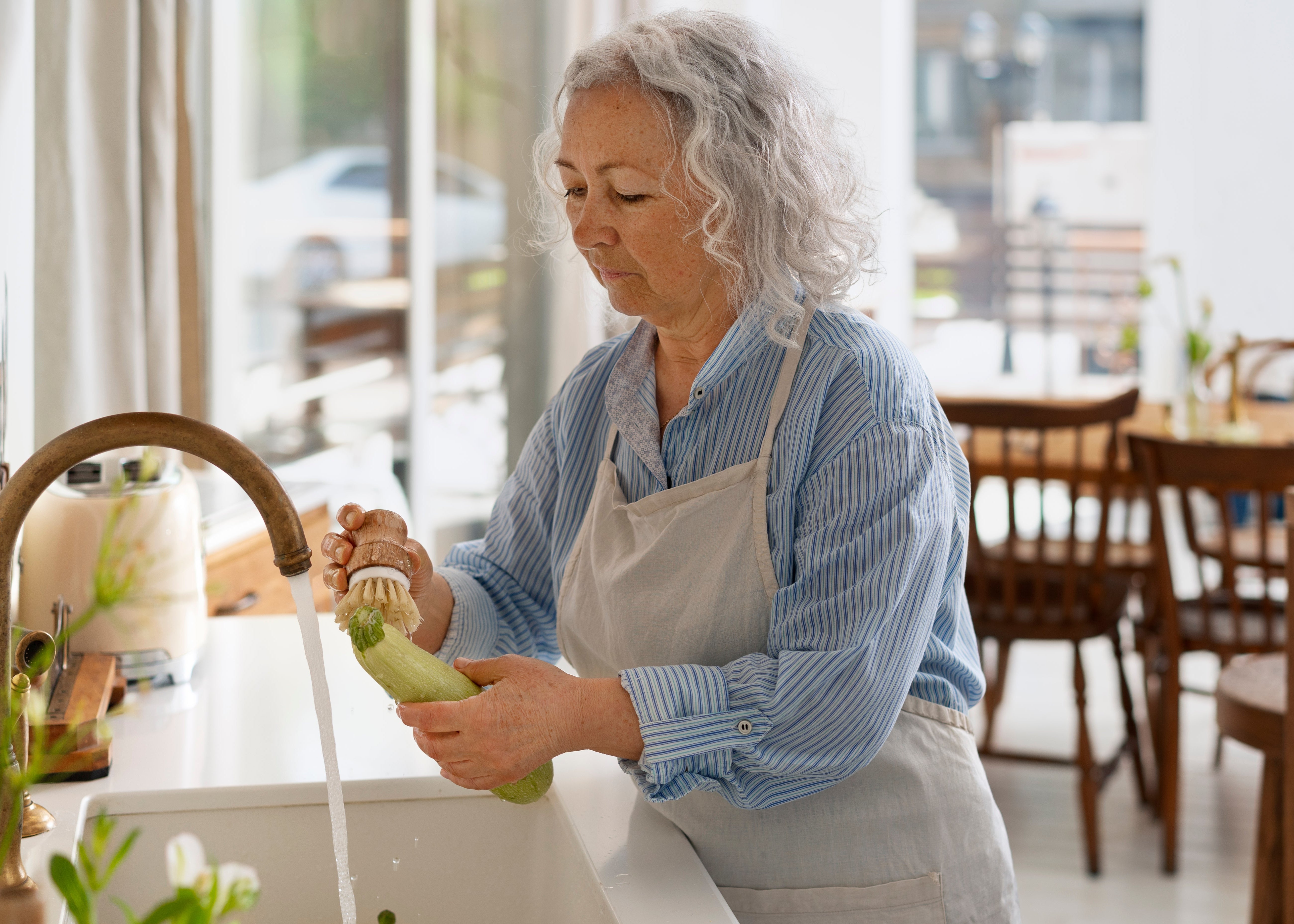 Woman washing vegetables in a kitchen sink with a neutral background