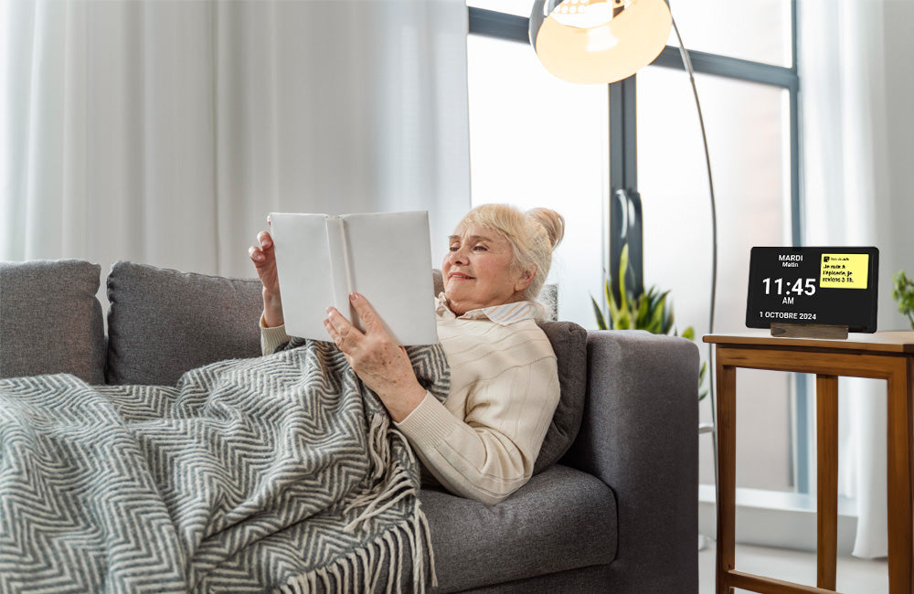 Une femme couchée sur un divan qui lit un livre avec l'horloge Idem sur sa table de chevet