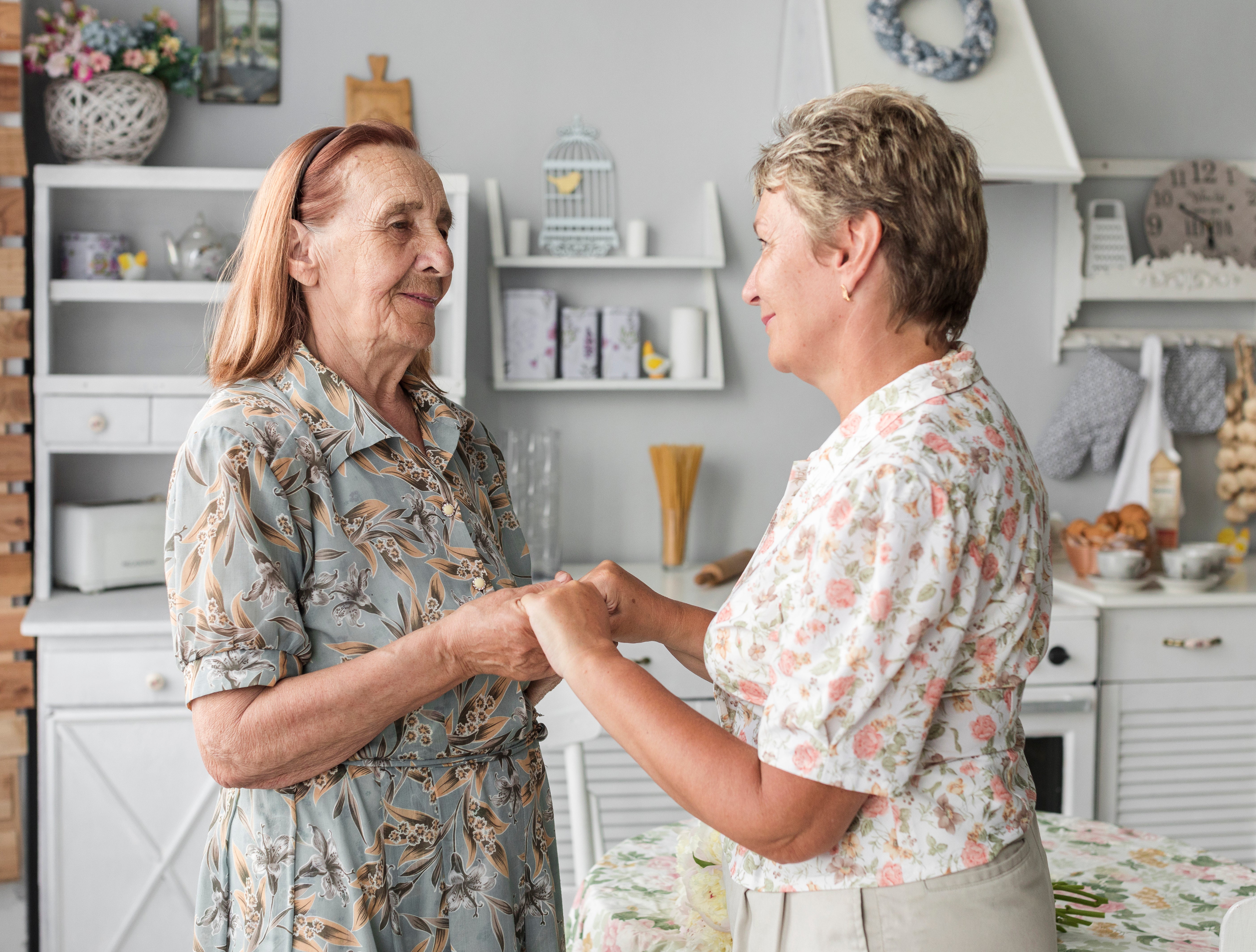 Two women in floral shirts shaking hands in a home setting.
