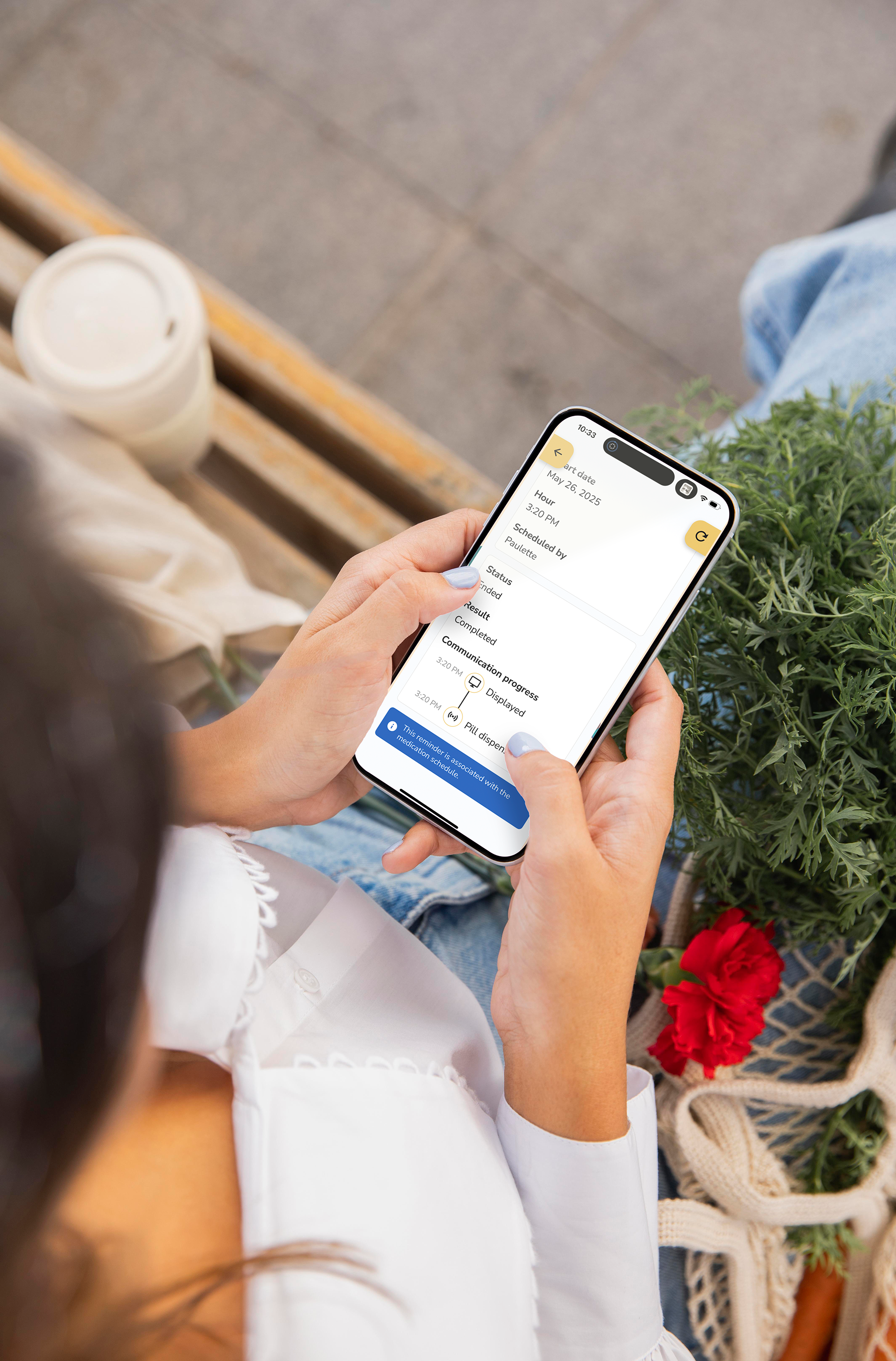 Person using a smartphone with the Idem Caregiver app outdoors with a plant and chair in the background